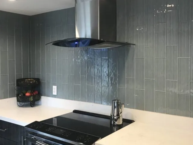 Glass subway tile backsplash in a modern kitchen with a dark countertop