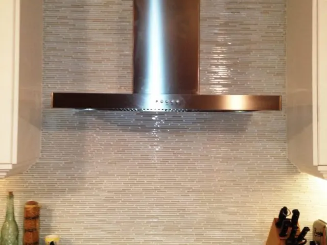 Stacked stone backsplash behind a range with stainless steel hood