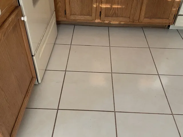 White kitchen tile floor with dark, dirty grout lines before cleaning