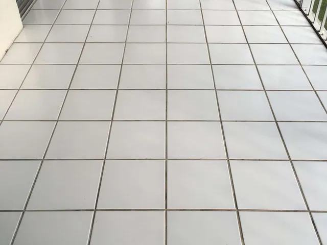 Beige ceramic tile floor with dark, uneven grout lines before color sealing