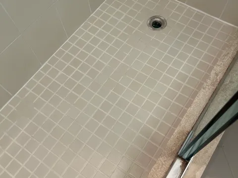 After: Mosaic shower floor with dark, moldy grout before and bright white grout after cleaning and sealing
