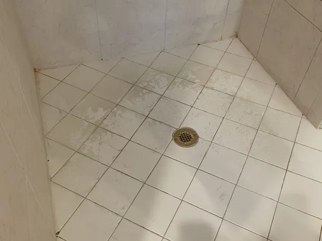Tiled shower floor and walls with aged, uneven grout