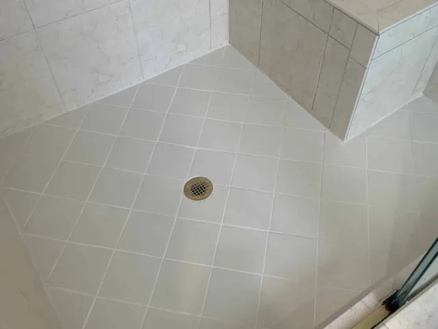 The same shower floor with clean white grout after regrouting
