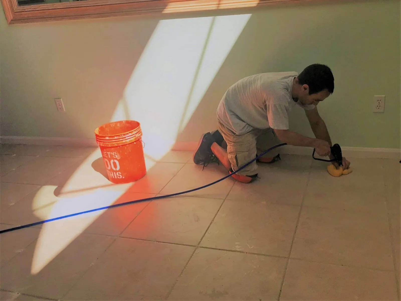 AAA Tile technician kneeling on a tile floor injecting bonding agent to re-bond hollow tiles