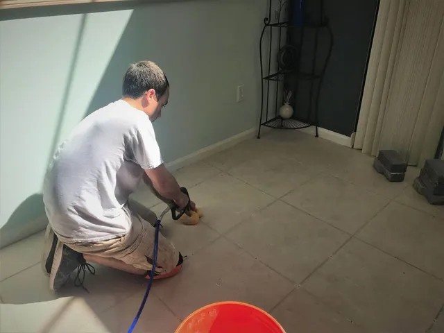 Technician kneeling on a living room tile floor during hollow tile repair