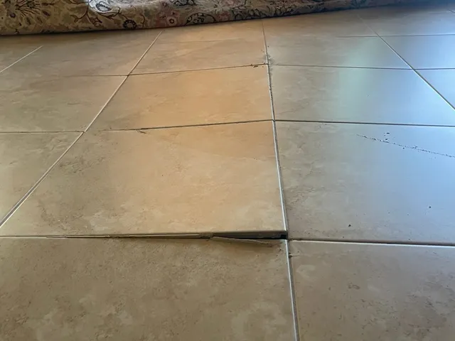 Raised floor tile with a cracked edge where two tiles have pushed against each other