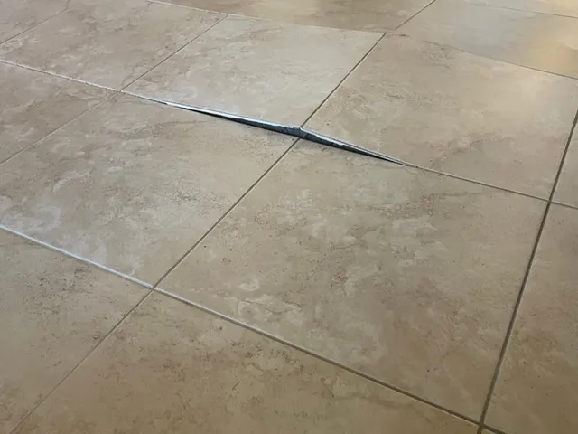 Two floor tiles peaked upward in a hallway, leaving a gap along the grout joint